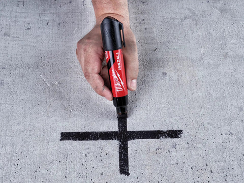 Hand using InkZall XL Chisel Tip Marker Black for Tough Jobs on concrete, demonstrating writing capability on dusty surfaces.