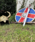 Kids Viking Horned Helmet For Costume Play LARP And Halloween on grass with shield, sword, and axe on a tree trunk.
