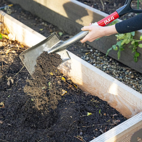 Compact Mini D Handle Square Head Shovel With Soft Grip lifting soil in garden bed, red and black finish, durable spade tool.