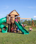 Children playing on Cedar Cove Wooden Swing Set With Spiral Tube Slide And Wave Slide, Elevated Clubhouse, and Swings in backyard.