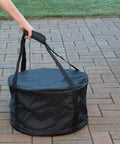 Person carrying Heininger Heavy-Duty Carry Bag For Portable Fire Pit on patio, showcasing vinyl material and sturdy handles.