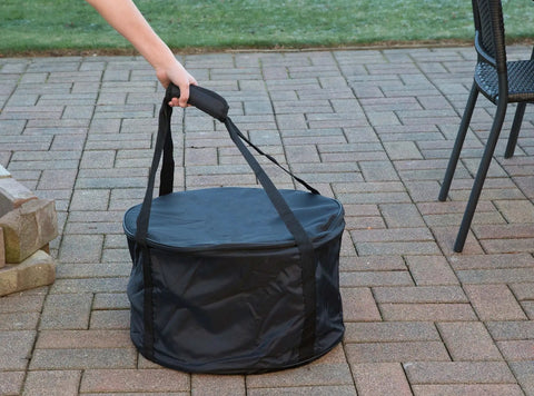 Person carrying Heininger Heavy-Duty Carry Bag For Portable Fire Pit on patio, showcasing vinyl material and sturdy handles.