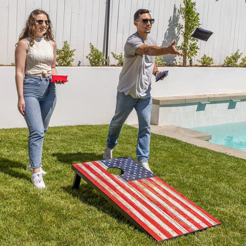 Couple playing with American Flag Regulation Size Cornhole Set with 2 regulation boards near a pool on grass in backyard