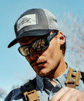 Man wearing Ballistic Rated Safety Glasses Featuring Matte Graphite Grey Frame And Tungsten Mirror Lenses outdoors.