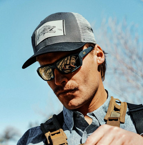 Man wearing Ballistic Rated Safety Glasses Featuring Matte Graphite Grey Frame And Tungsten Mirror Lenses outdoors.