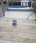 A person applying Hardcore Textured Deck Coating White 5 Gallon Waterproof Non Skid Sealant on a wooden deck.