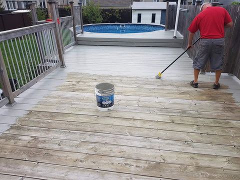 A person applying Hardcore Textured Deck Coating White 5 Gallon Waterproof Non Skid Sealant on a wooden deck.