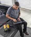 Man using laptop powered by 1000W Car Power Inverter With LCD Display Dual 120V AC Outlets Three Point One Amp USB Ports 12V DC Adapter.