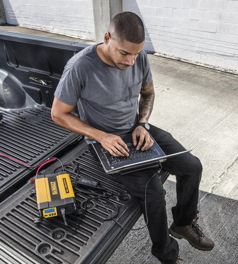 Man using laptop powered by 1000W Car Power Inverter With LCD Display Dual 120V AC Outlets Three Point One Amp USB Ports 12V DC Adapter.