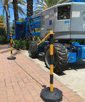 Two Pack Traffic Delineator Poles With Chain Included Portable Fillable Base No More Cones For Parking Lots Construction Sites Road Markers Street Stanchions Black Yellow positioned in front of construction equipment on paved ground.