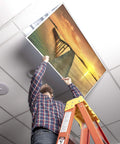 Person installing 2x4 Fluorescent Light Covers For Classroom Ceiling Fixtures Beach Vibe 4 Pack, showing sunset beach design.