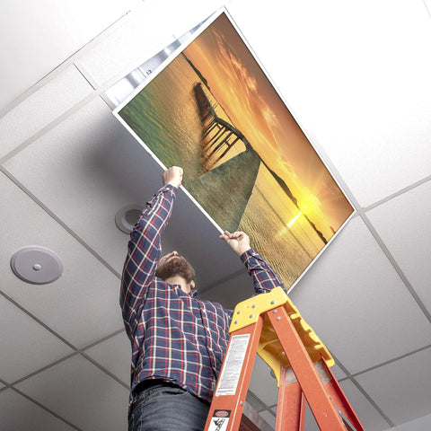 Person installing 2x4 Fluorescent Light Covers For Classroom Ceiling Fixtures Beach Vibe 4 Pack, showing sunset beach design.