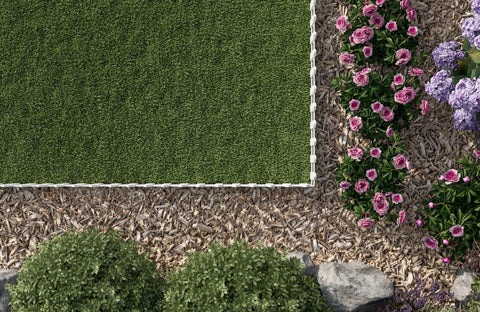 Top view of Picket Border Fence Kit 24.9 Foot White Outdoor Garden Fence in a yard, with grass, flowers, and decorative wood chips.