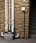 Rugged Duplex Grinder Waste Pump Unit 1 Horsepower Lift Station for Commercial Sites with pipes and lift station installed on brick wall.