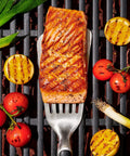 Grilling Tool Precision Turner For Effortless Burger Flips And Flaky Fish Fillets With Thin Beveled Head Non Slip Grip And Hanging Ring OXO Good Grips Black, lifting grilled salmon on a barbecue.