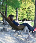 Person relaxing in Underbelly Gear Sling Hammock For Camp Gear Storage, Lightweight And Portable Mini Hammock, outdoors OD green.