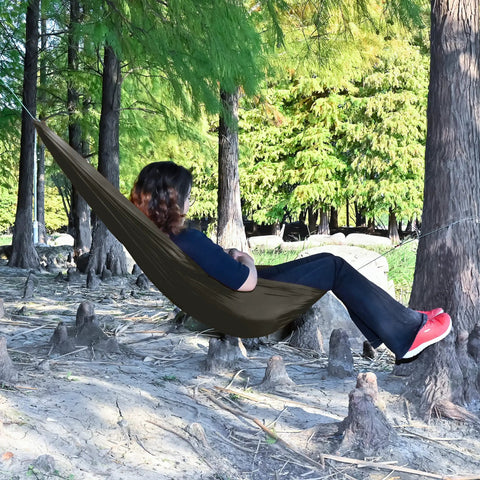 Person relaxing in Underbelly Gear Sling Hammock For Camp Gear Storage, Lightweight And Portable Mini Hammock, outdoors OD green.