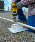 Front view of worker installing a white PVC rooftop conduit support on a gravel roof using a yellow drill.