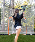 Lacrosse Goal Backstop Net No More Chasing Balls 12 Foot By 9 Foot For Backyard Practice Keeps Balls In Play Built Tough With Weather Resistant Polyester And Easy Setup Fibertech visible in backyard with person practicing lacrosse.