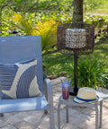 Rustic Tanglewood Outdoor Table Lamp with oil rubbed bronze, woven rattan shade, next to patio chair on brick surface