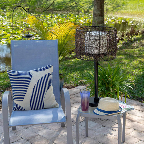 Rustic Tanglewood Outdoor Table Lamp with oil rubbed bronze, woven rattan shade, next to patio chair on brick surface