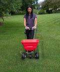 Person using Big 80lb Capacity Broadcast Spreader for lawns and seeds with rustproof poly hopper on large yard.