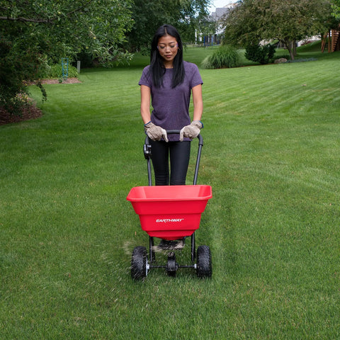 Person using Big 80lb Capacity Broadcast Spreader for lawns and seeds with rustproof poly hopper on large yard.