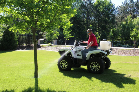 Person using 9 Gallon UTV And ATV Spot Sprayer with Everflo 1.0 GPM pump, spraying tree from a vehicle in a grassy area