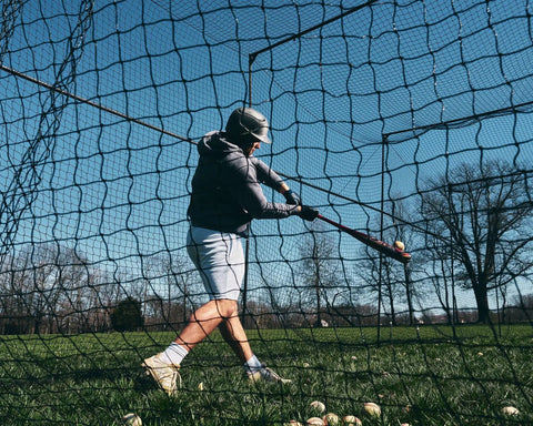 Man practicing in 40 Ft Baseball Softball Batting Cage With Black Steel Frame And 60 Ply Net, grass and trees in background.