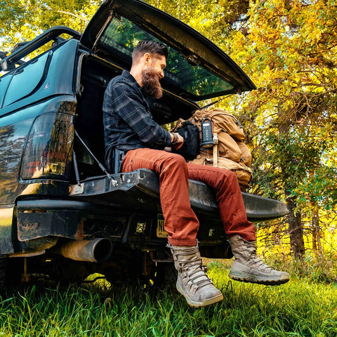 Man sitting on truck tailgate holding Rechargeable Solar Powered Flashlight Lantern For Camping And Outdoors USB And Solar Charging Emergency Power Bank Lifesaver Lantern For Power Outages Hiking And Survival Car Camping Essential.