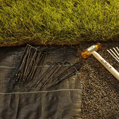 100 Pack 6 Inch 11 Gauge Heavy Duty U Shaped Garden Staples Ground Stakes For Anchoring Landscape Fabric Spikes Pins Pegs Pro Grade Lawn Landscaping Tools, shown on landscape fabric near grass.