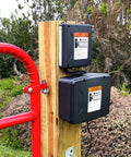 Workhorse 12 Volt 7 Ah Sealed Lead Acid Battery And Rugged Weatherproof Enclosure Kit mounted on wooden post next to red gate.