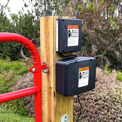 Workhorse 12 Volt 7 Ah Sealed Lead Acid Battery And Rugged Weatherproof Enclosure Kit mounted on wooden post next to red gate.