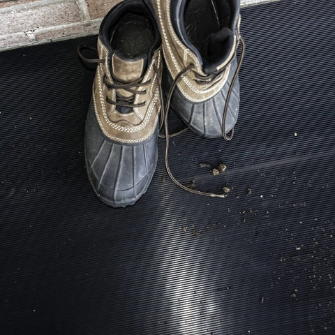 Tough As Nails Vinyl V Groove Floor Mats For Garages Shops And Commercial Spots Oil Grease Chemical Resistant Non Slip Anti Fatigue Mat In Black One Eight By Twenty Four By Sixty Inches with muddy shoes on the mat.