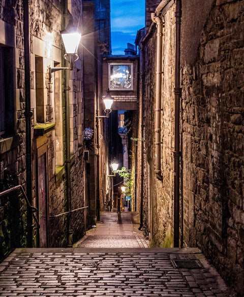 Narrow cobblestone alleyway with warm streetlights illuminating stone buildings at dusk