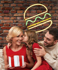 Family celebrating under a burger neon sign on brick wall background, woman holding gift box