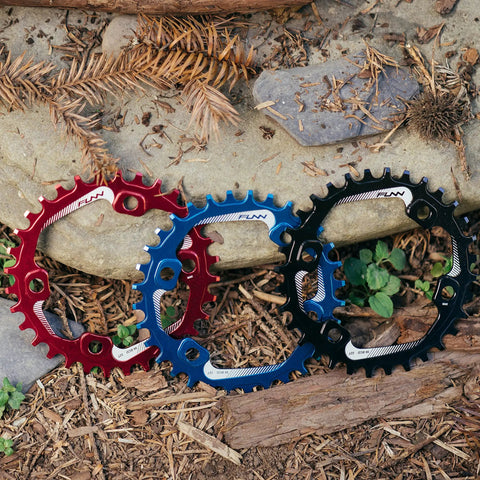 Red, blue, and black 34T Narrow Wide Chainring For 9 To 12 Speed Cranks Asymmetric 96mm BCD Interface in durable alloy on rocky trail.