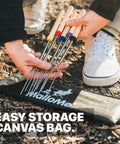 Person holding 5-pack of long 32 inch smores sticks kit with stainless steel skewers and smooth wooden handles for marshmallow roasting at the campfire fire pit gear for outdoor camping durable essentials with canvas storage bag on ground.