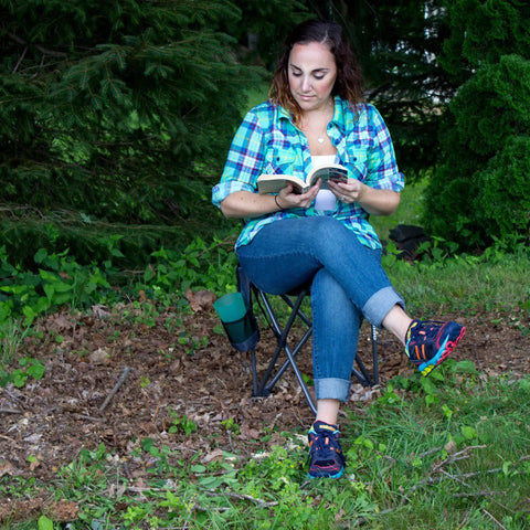 Woman reading on Quik-E-Seat Portable Folding Tripod Chair with drink holder at outdoor event
