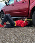 Person using VersaMat Roll Up Workhorse High Density Foam Utility Mat Black for Garage and Home under a red truck