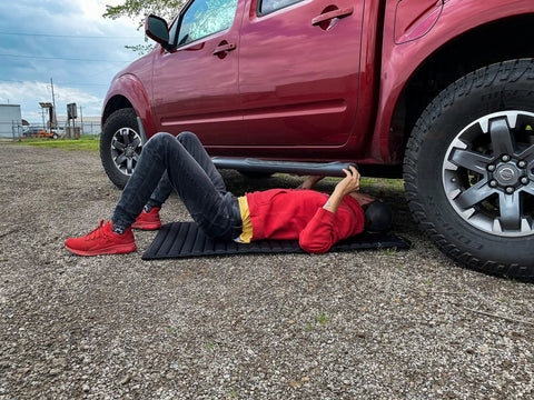 Person using VersaMat Roll Up Workhorse High Density Foam Utility Mat Black for Garage and Home under a red truck