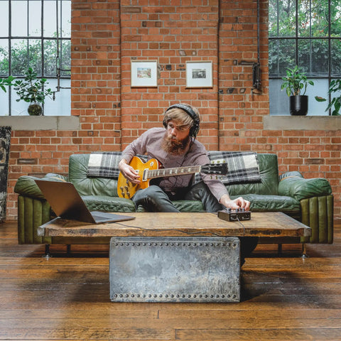 Man using iD4 MkII Audio Interface With Class A Mic Preamps, USB C on coffee table, playing guitar in loft studio, brick wall background