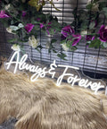 Forever Neon Sign For Weddings And Parties, Cold White LED Wall Decor laying on fur with floral and grid backdrop.