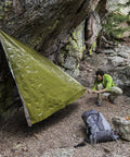 Person setting up a 90 Percent Heat Reflective Emergency Blanket Beefed Up Heavy Duty For Disaster Prep Kit as a makeshift shelter outdoors.