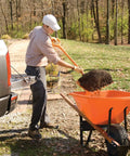 Man using All Poly Scoop Fork with 8 tines and D Grip handle to load mulch into a wheelbarrow in a garden setting