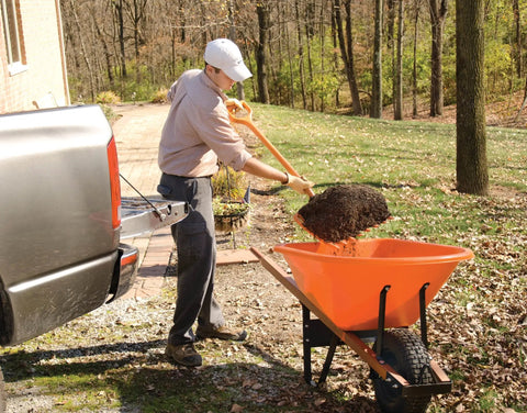 Man using All Poly Scoop Fork with 8 tines and D Grip handle to load mulch into a wheelbarrow in a garden setting
