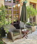 Outdoor patio seating area with two wicker chairs, green cushions, a round table, and an umbrella, surrounded by plants and lanterns.