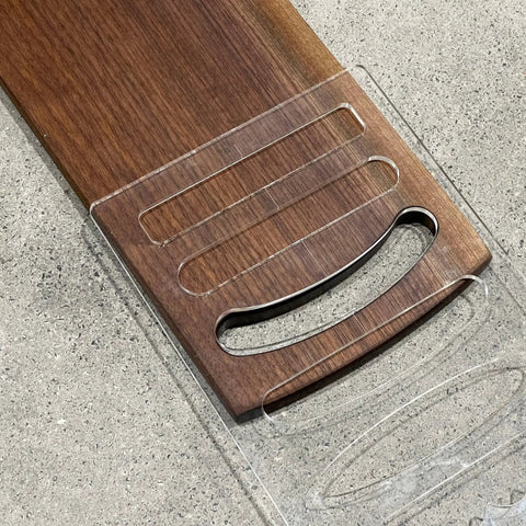 Six In One Charcuterie Board Handle Template Acrylic Router Guide placed on a wooden cutting board for carving smooth grips.