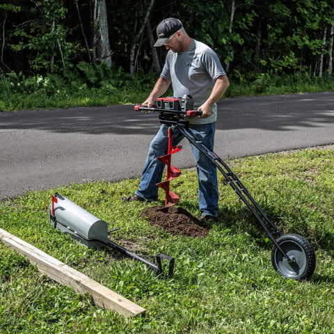 Man using 60V Cordless Dirt Auger with 8 Inch High Performance Bit near road, grass, and tools; drilling hole in lawn.