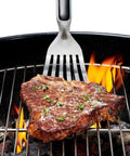 Grilling Tool Precision Turner flipping steak over grill with thin beveled head, non-slip grip, and hanging ring, OXO Good Grips Black